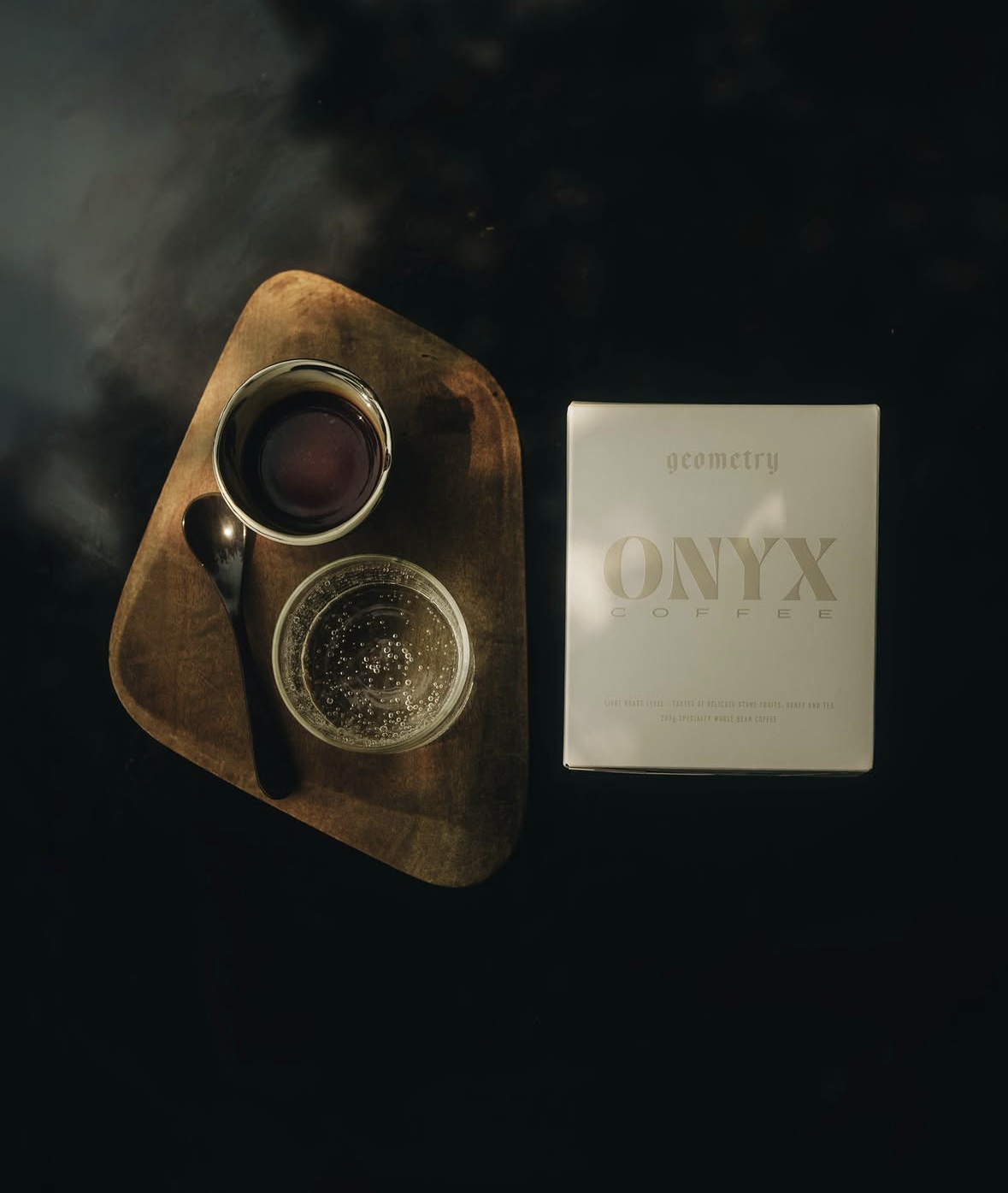 Onyx Coffee Lab — a cup of espresso and a glass of sparkling water on a wooden tray beside an Onyx Coffee geometry bag