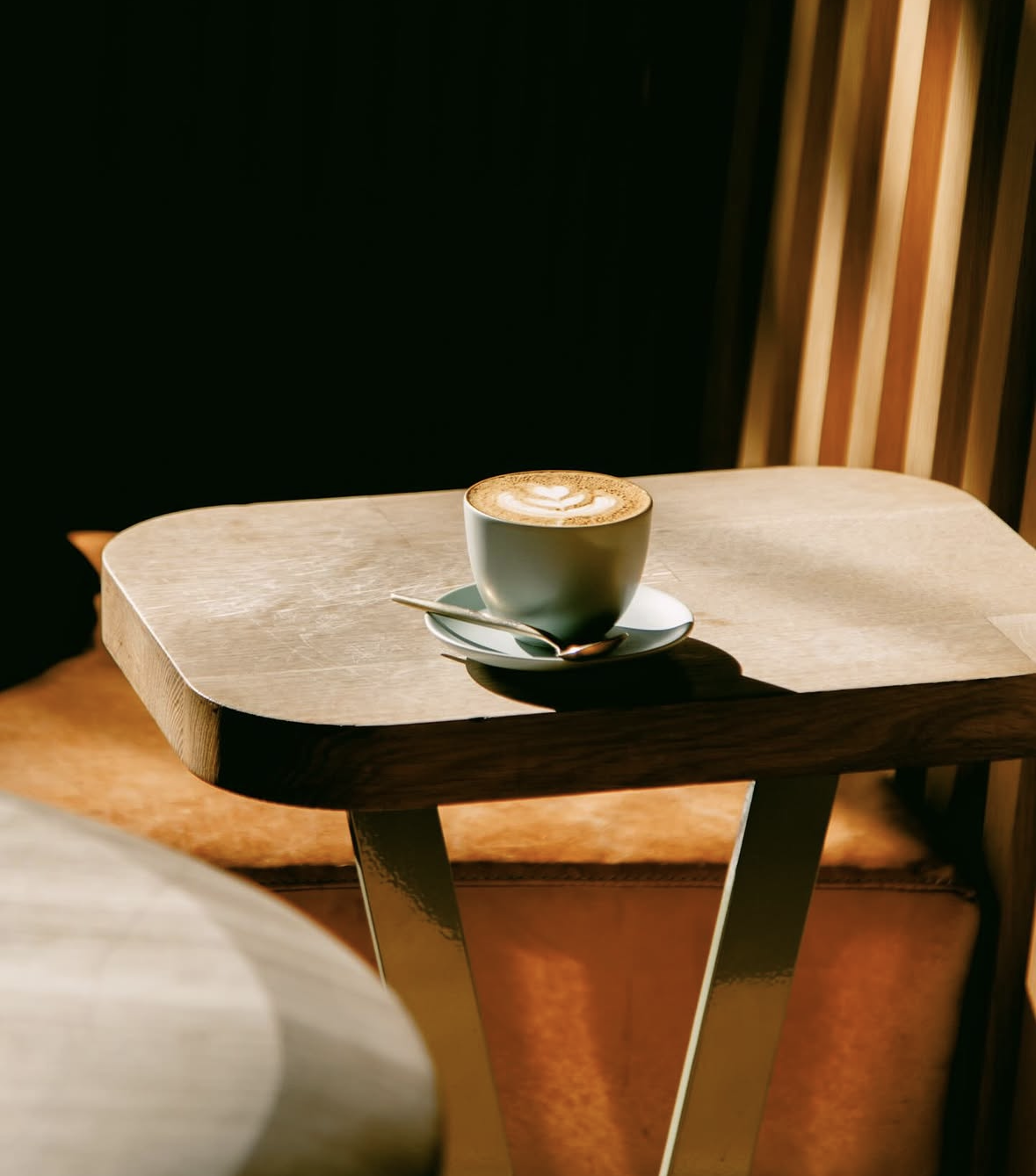 Verve Coffee Roasters — a latte in a grey ceramic cup on a saucer atop a wooden table, bathed in warm afternoon light