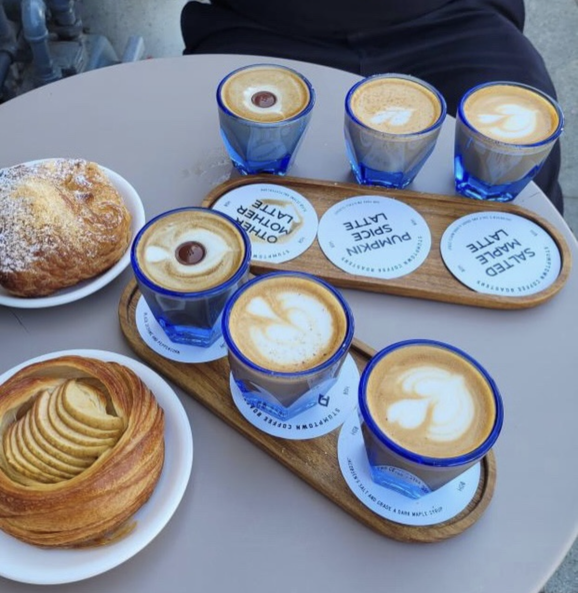 Stumptown Coffee Roasters — a tray of lattes in blue-rimmed glasses beside pastries on a café table