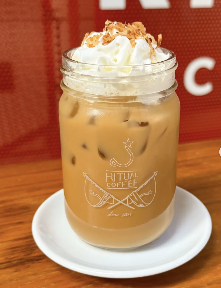Ritual Coffee Roasters — an iced latte in a branded mason jar glass topped with whipped cream and toasted coconut, on a white saucer